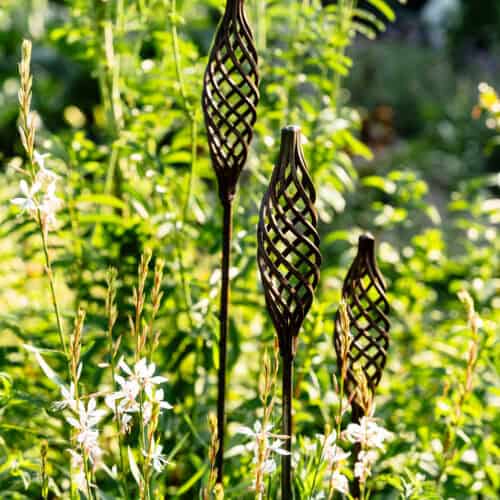 Fűszernövények és kerti dekorációk a Patinakertben, napfényes kertkörnyezetben.