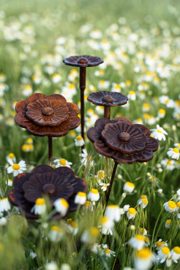 Alt text: Rustikális fa virágtartó virágmintás kertben, virágos mező hátterével.