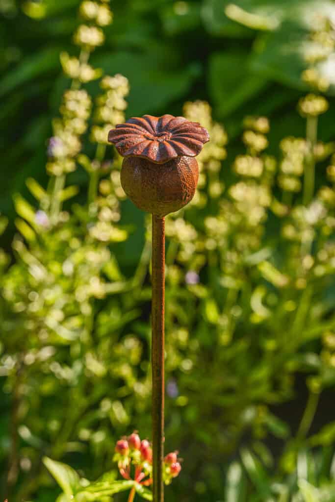 Részlet egy réz szoborról, mely kertben áll, zöld növények között.