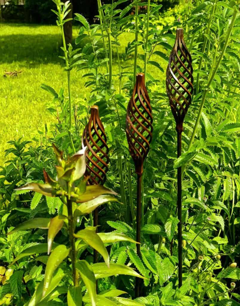 Zöld növények és rozsdás, mintás fából készült kert díszek, természetes kert kialakítás.