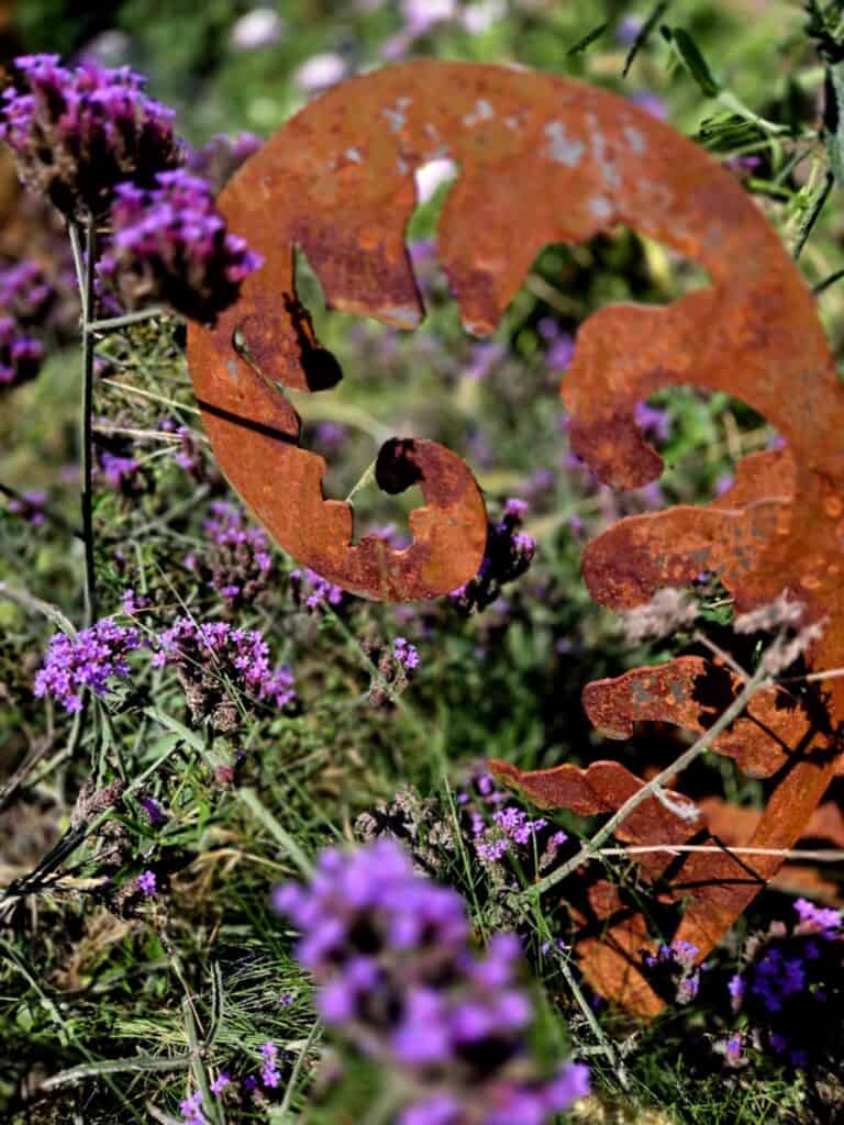 Rőt vas dísztárgy természetes környezetben, virágos mezőn, őszi hangulat.