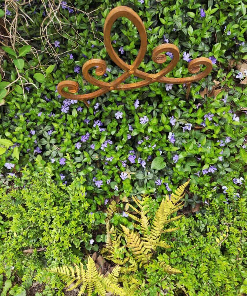 Színes növények és kovácsoltvas dísz a kertben, zöld és lila árnyalatokkal, természetes kertészeti d.