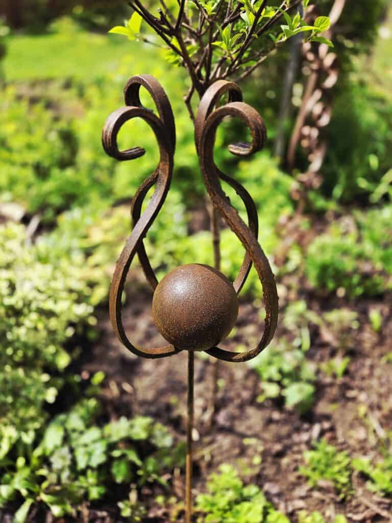 Fémképző művészeti dekoráció kertben, növények között. Kézműves vas szobor, modern kertészeti dísz,.