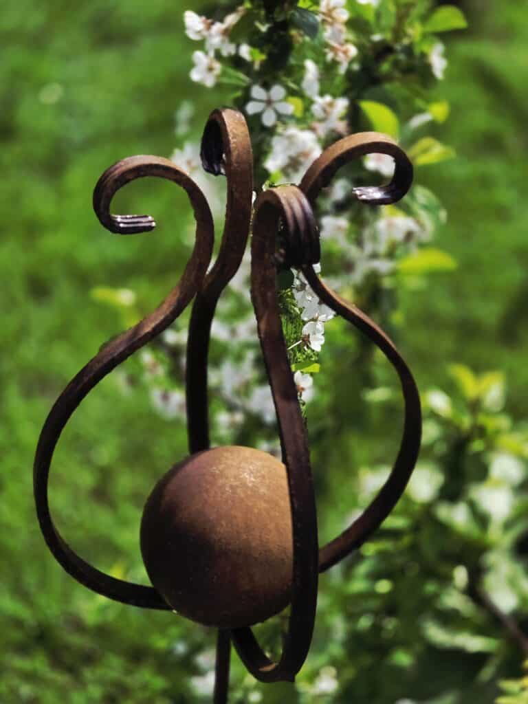 Védett kertkapu kovácsoltvas díszítéssel, virágzó növényekkel háttérben.